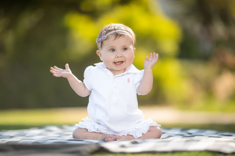 Kira sitting on a blanket with her hands up in the air