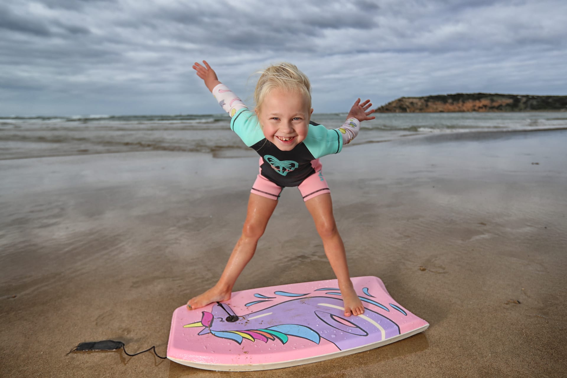 Quinnie standing on her boogie board on the sandat the beach