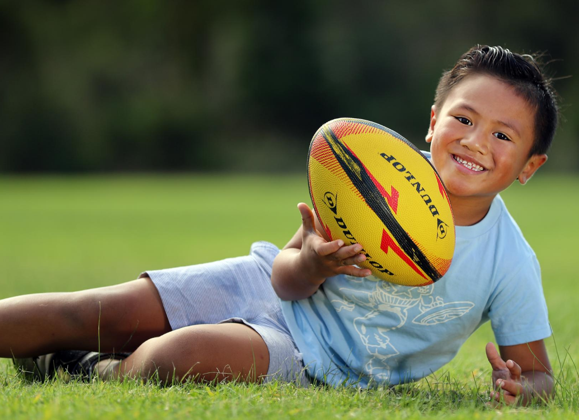 Maddox lying on the grass holding a rugby ball