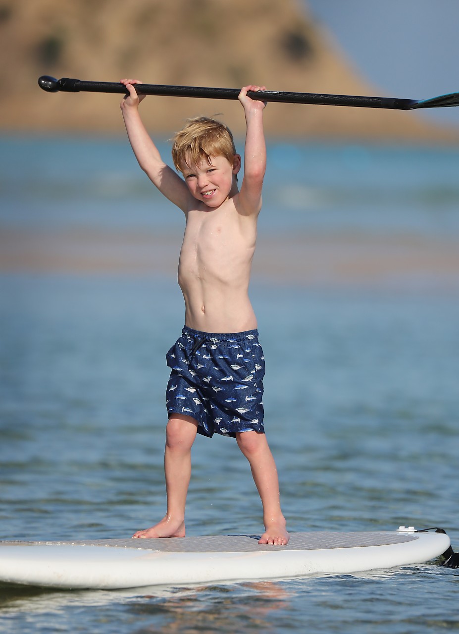 Harry Munro standing on a stand up paddle board in the ocean, holding the paddle above his heard