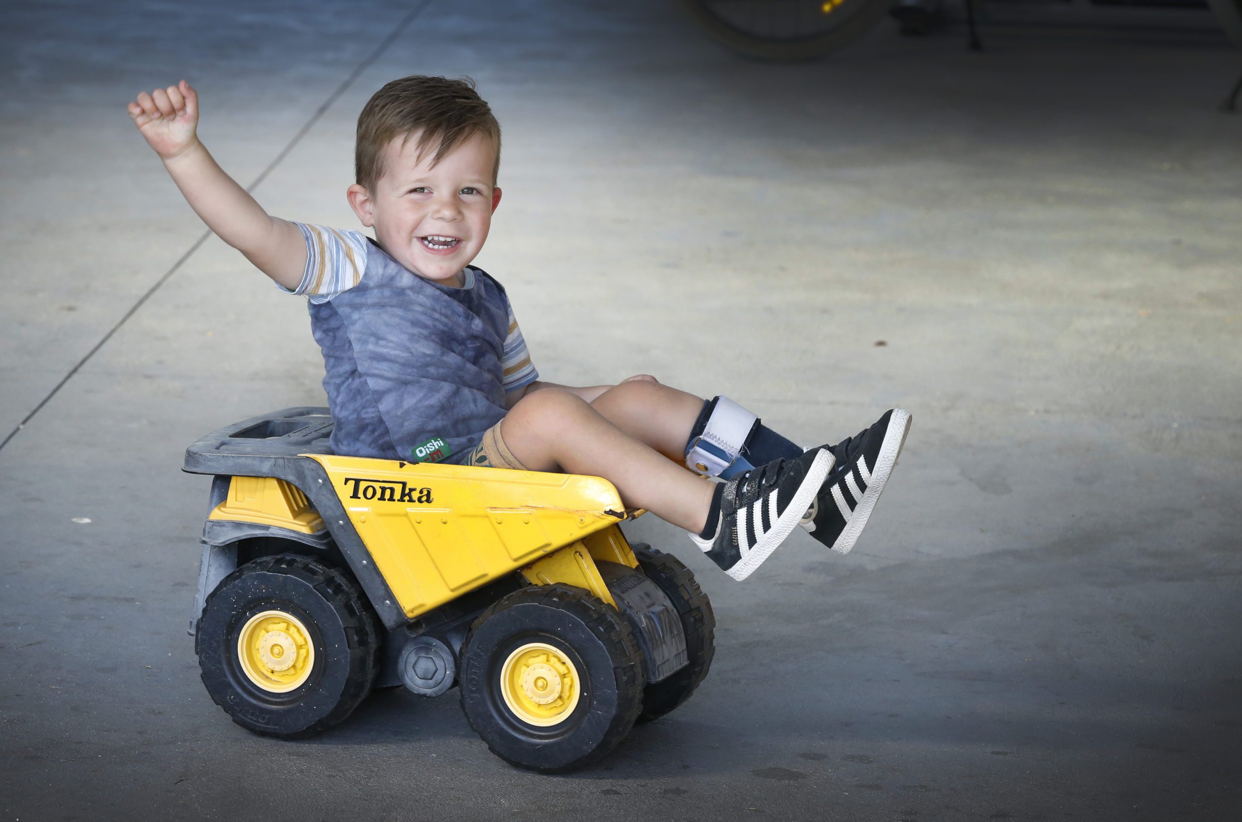 Malu sitting in a toy truck, smiling with his arm raised up in the air