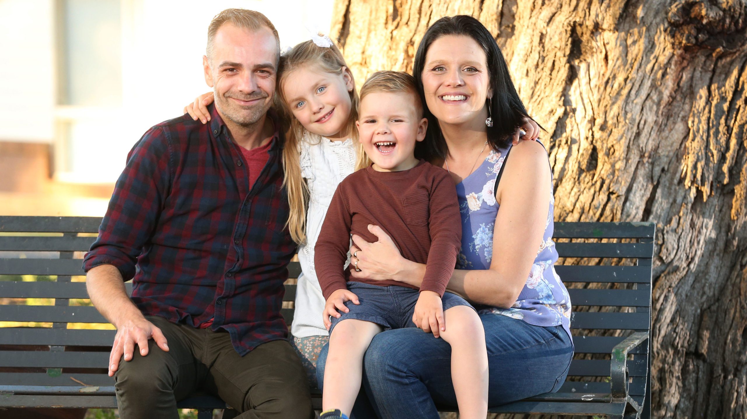 Parents Jason and Alex sitting on a park bench with William and his sister Zoe