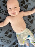 Baby Ronin lying on his back. He is smiling and his arms are out beside him.