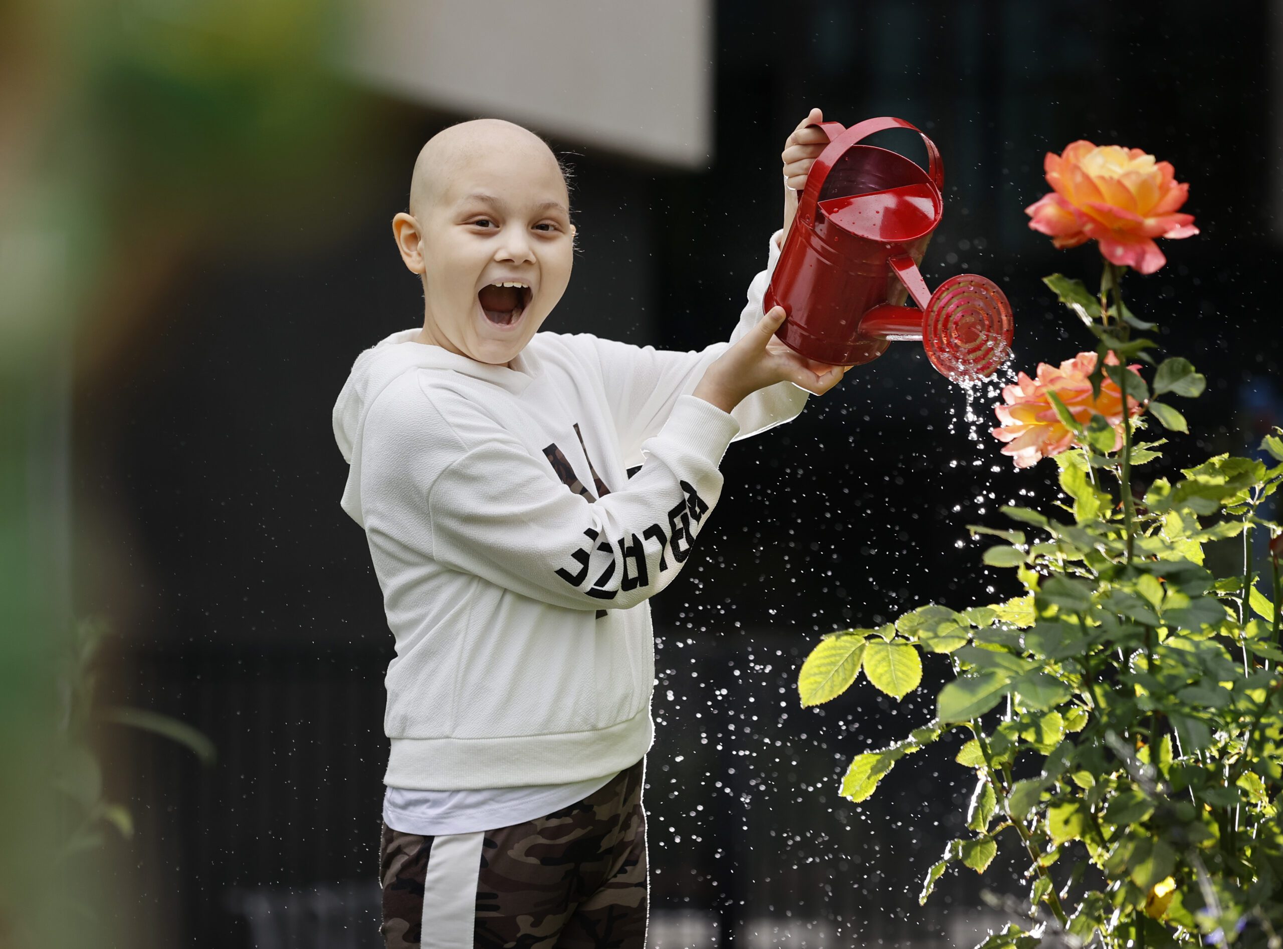 Aliyana watering flowers with a water can. Aliyana is bald for cancer treatment