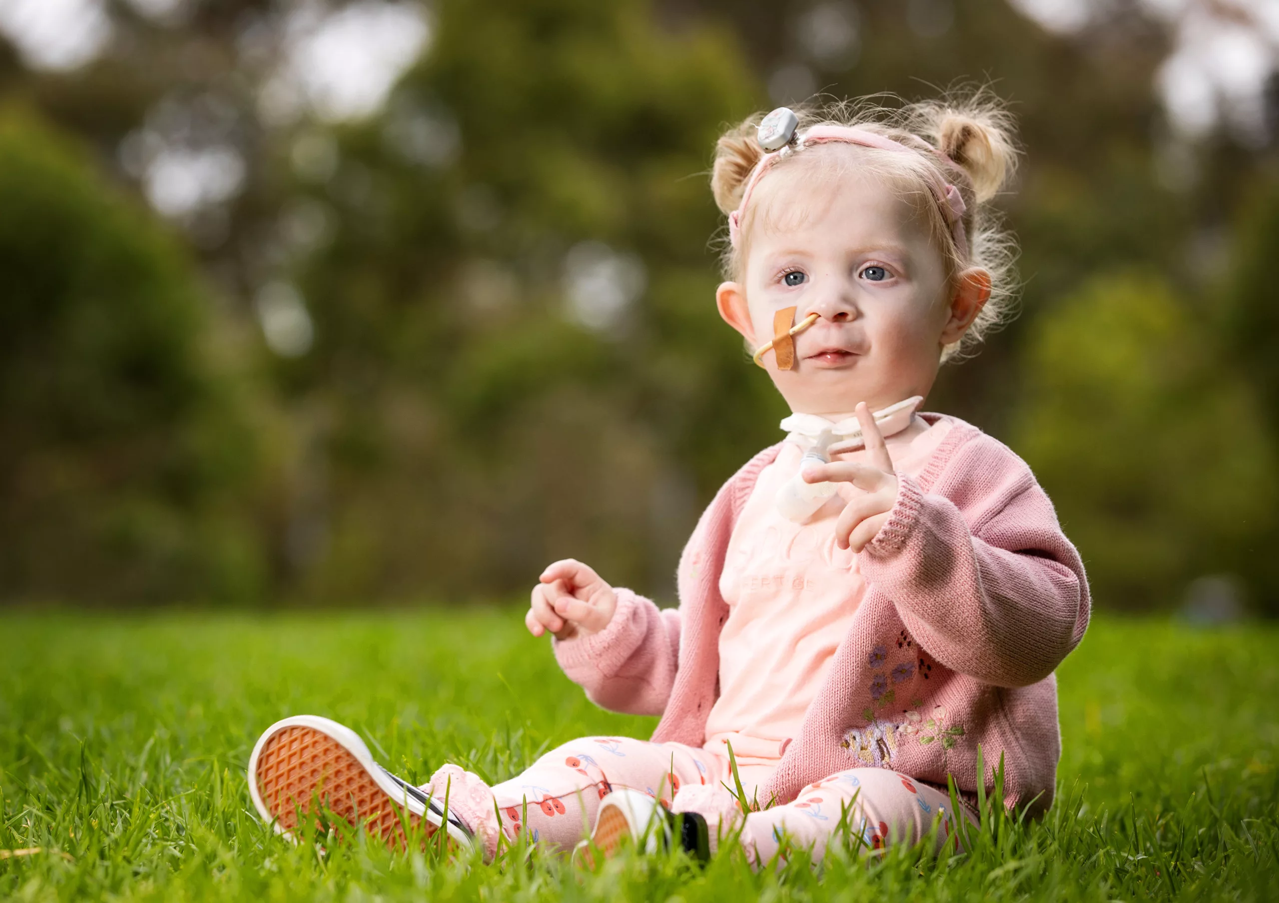 Kaiah sitting on the grass outside in an adorable pink outfit