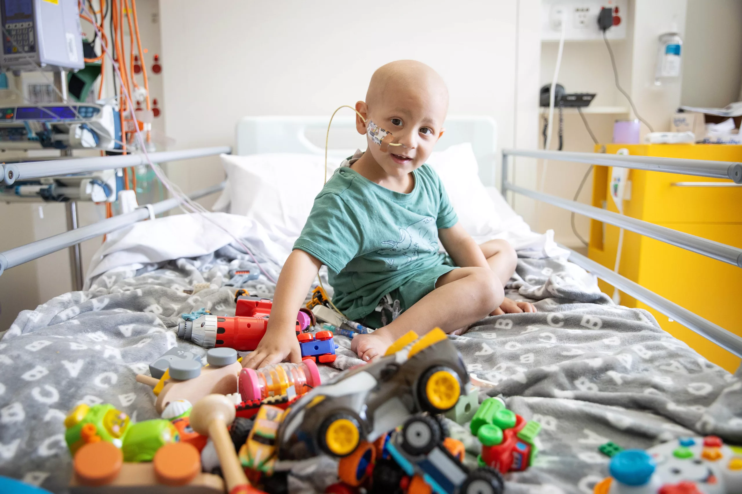 Ibrahim sits on a hospital bed at the rch melbourne in a light blue shirt playing with toy trucks and cars.