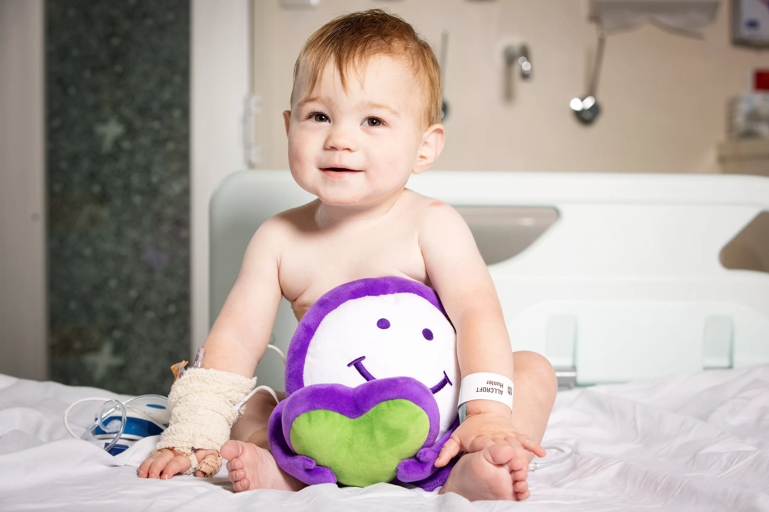 Hunter sits on a bed at the Royal Childrens hospital Melbourne with a Welbie plushie