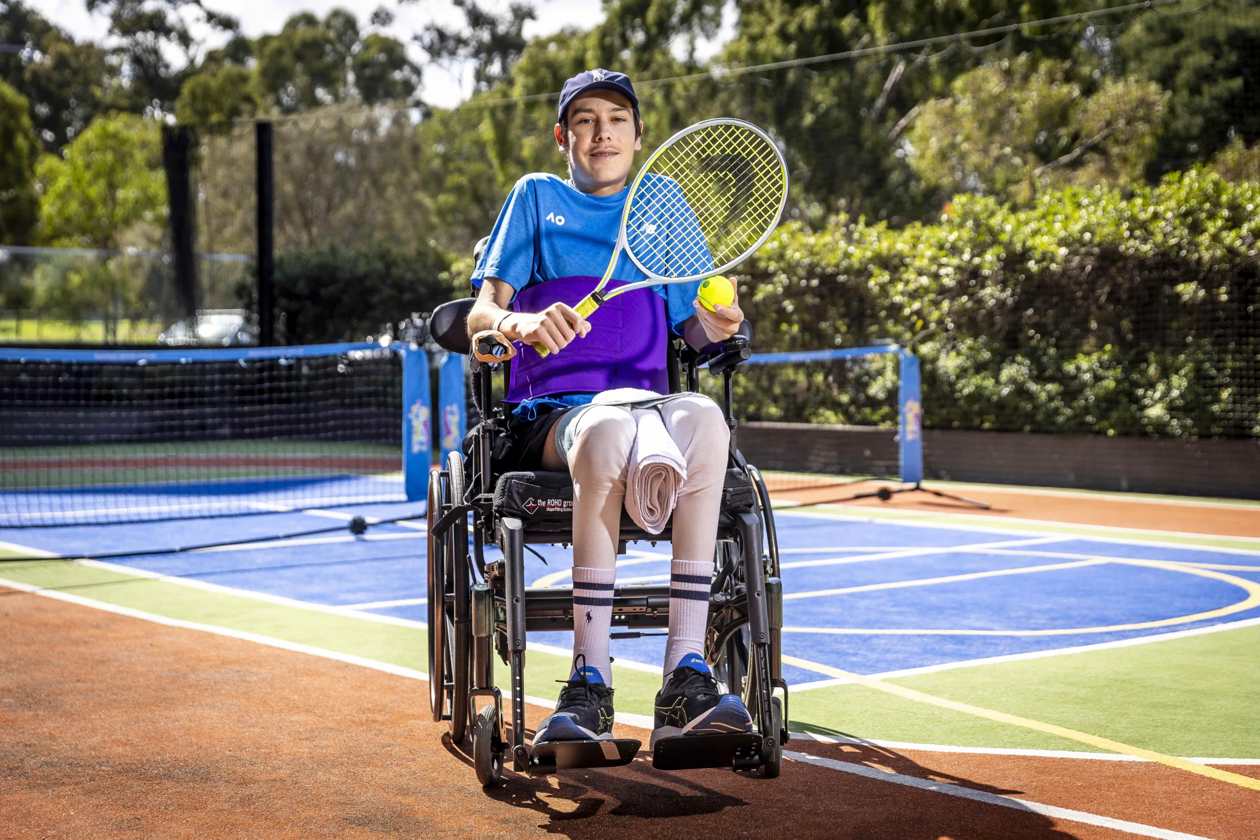 Patient in a wheelchair holding a tennis racquet, on a tennis court.